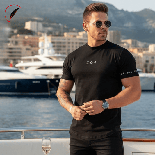 A man wearing a black short-sleeve t-shirt with '304' printed on the chest and sleeve, standing on a yacht with a marina and mountains in the background.