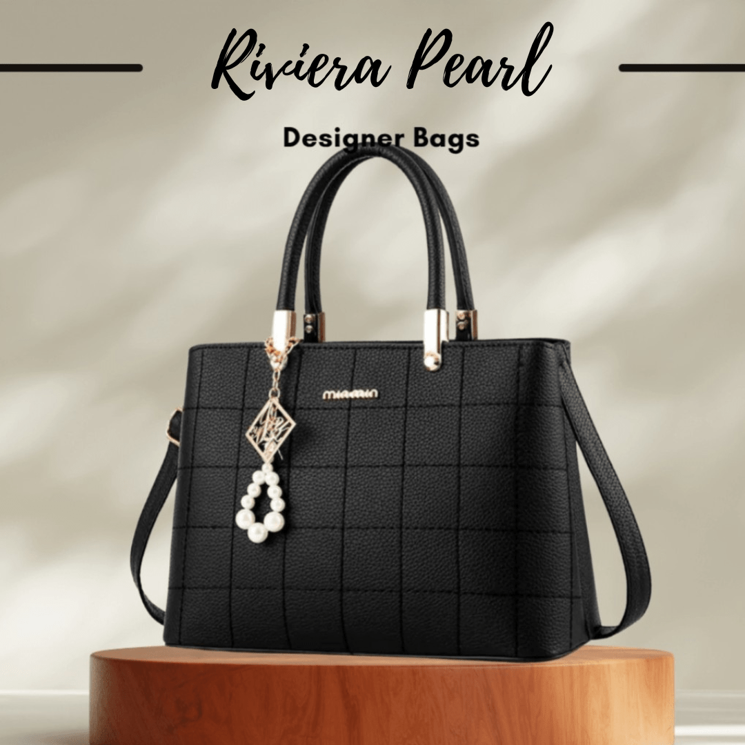 A black textured tote handbag with double top handles, a shoulder strap, and a pearl-bead hanging charm, displayed on a wooden pedestal with the text 'Riviera Pearl Designer Bags' above it.