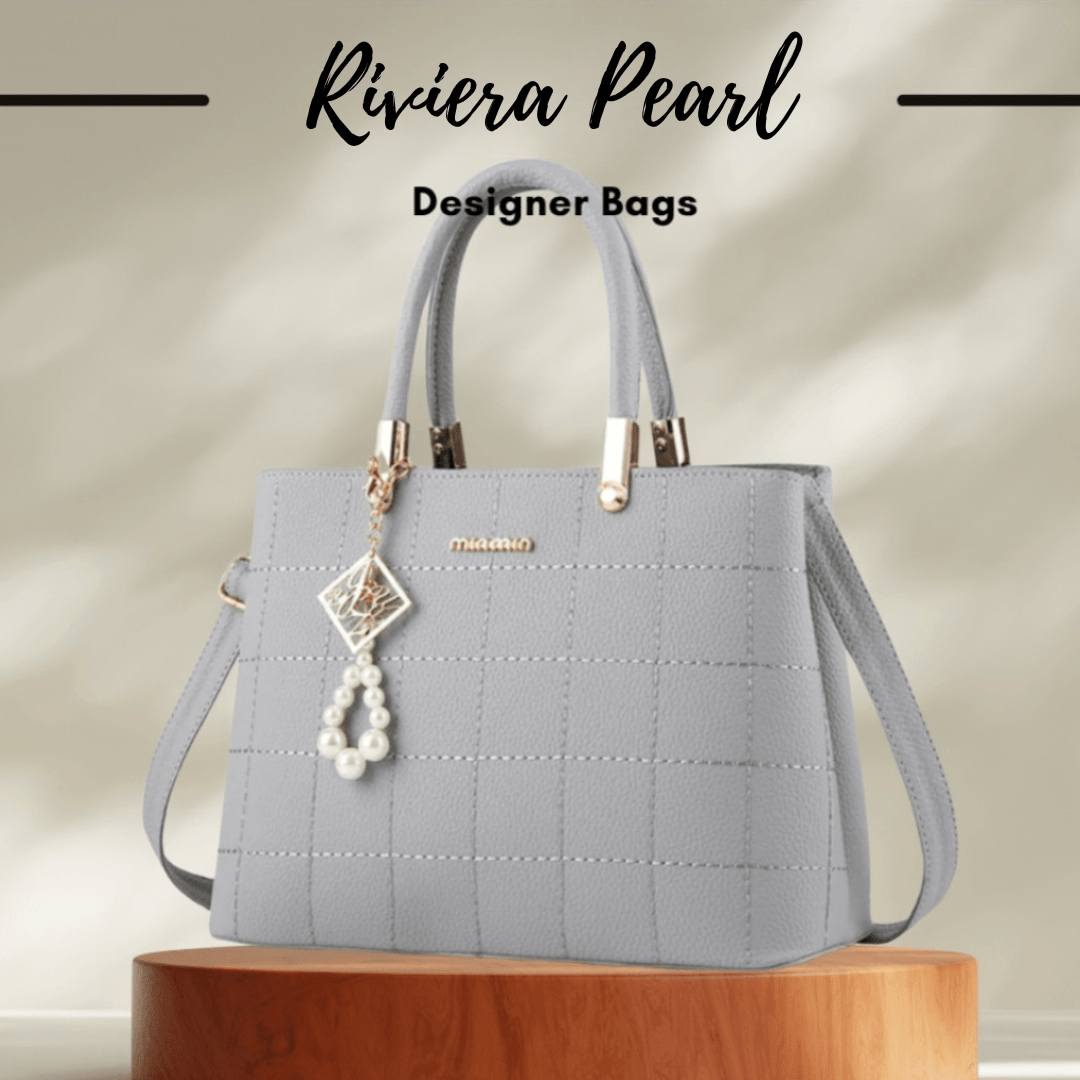A light gray designer handbag with a quilted texture, dual top handles, a detachable shoulder strap, and a dangling pearl charm, displayed on a wooden pedestal with the text 'Riviera Pearl Designer Bags' above it.
