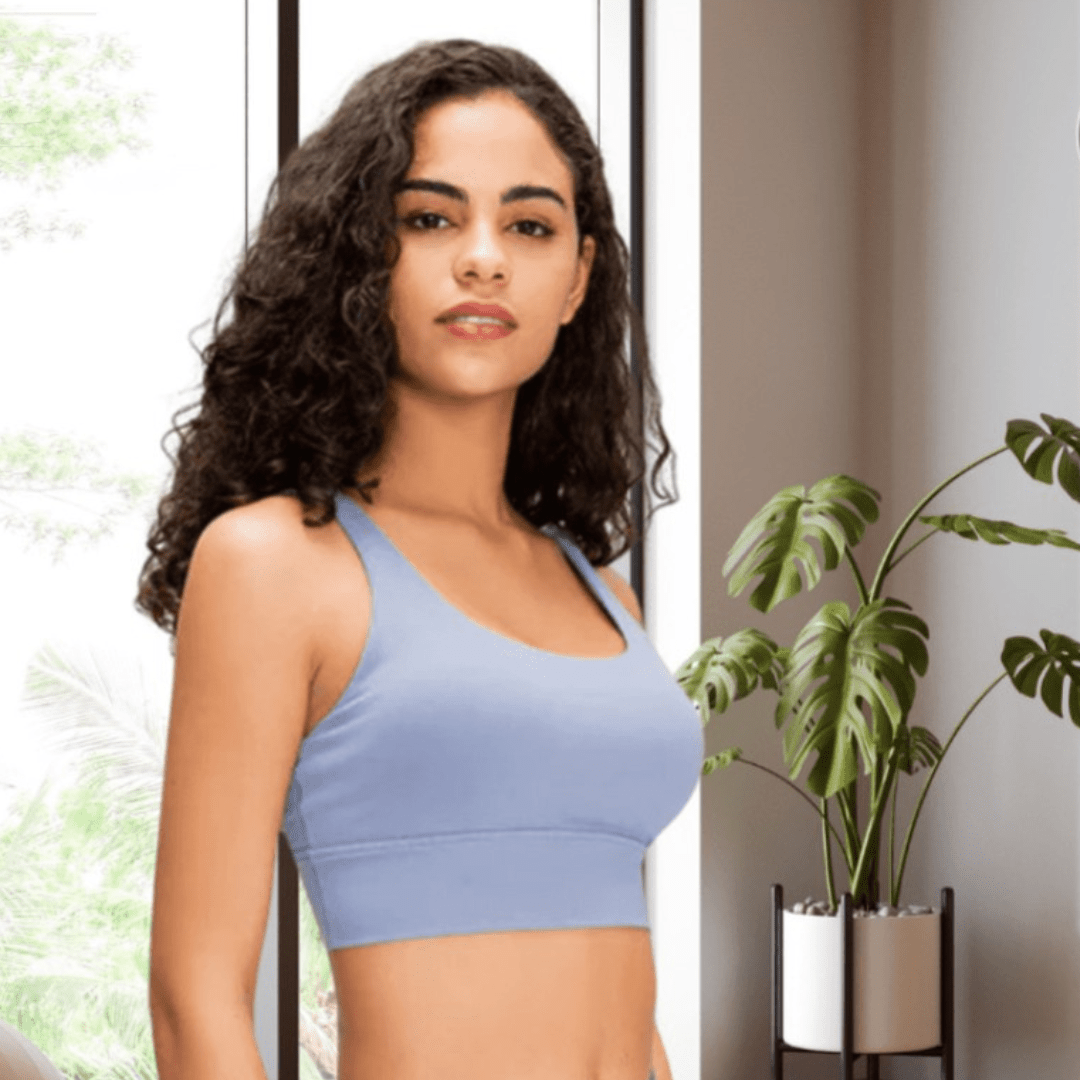 Woman wearing a light blue sports bra in a home setting with a plant.
