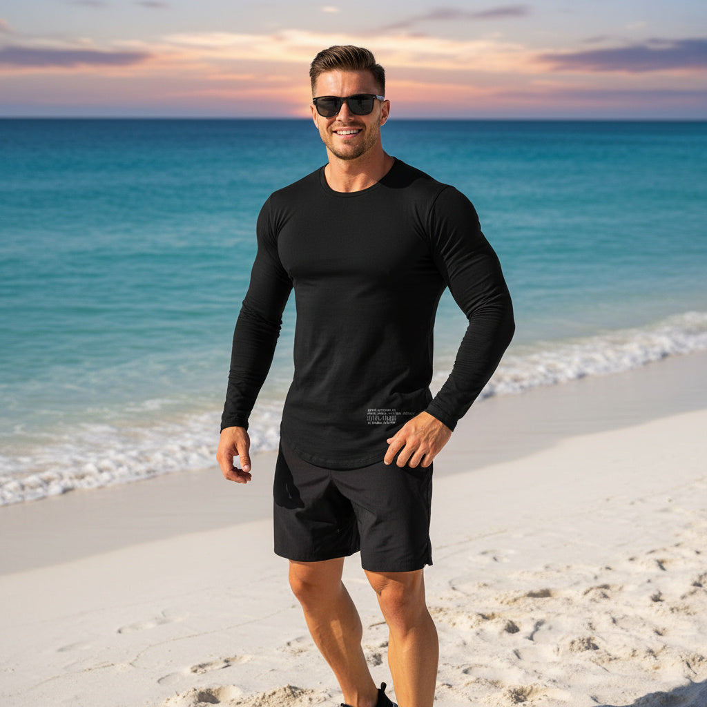 Man wearing a black long-sleeve shirt and shorts on a beach at sunset.