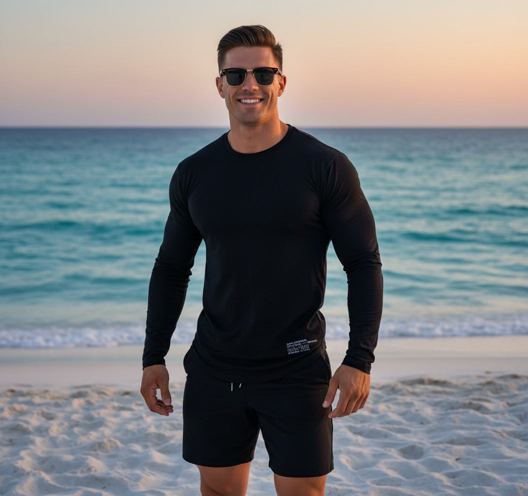 Man wearing sunglasses and black clothing standing on a beach with ocean in the background
