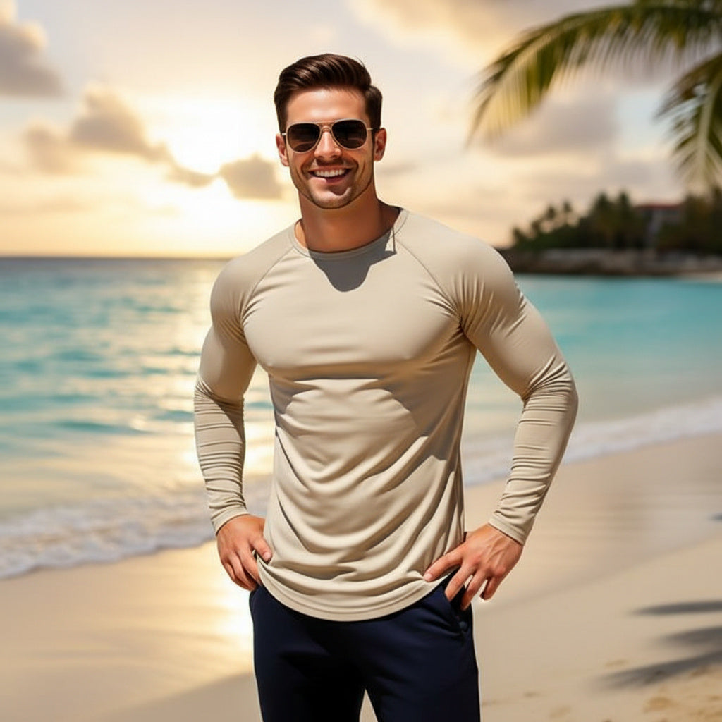 Man wearing sunglasses and a beige long-sleeve shirt on a beach with palm trees and ocean in the background.