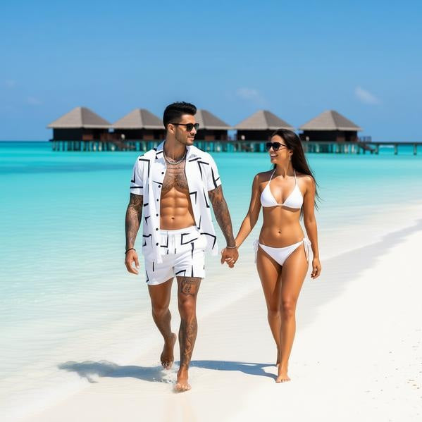 Man and woman walking on a tropical beach with clear blue water and huts in the background.
