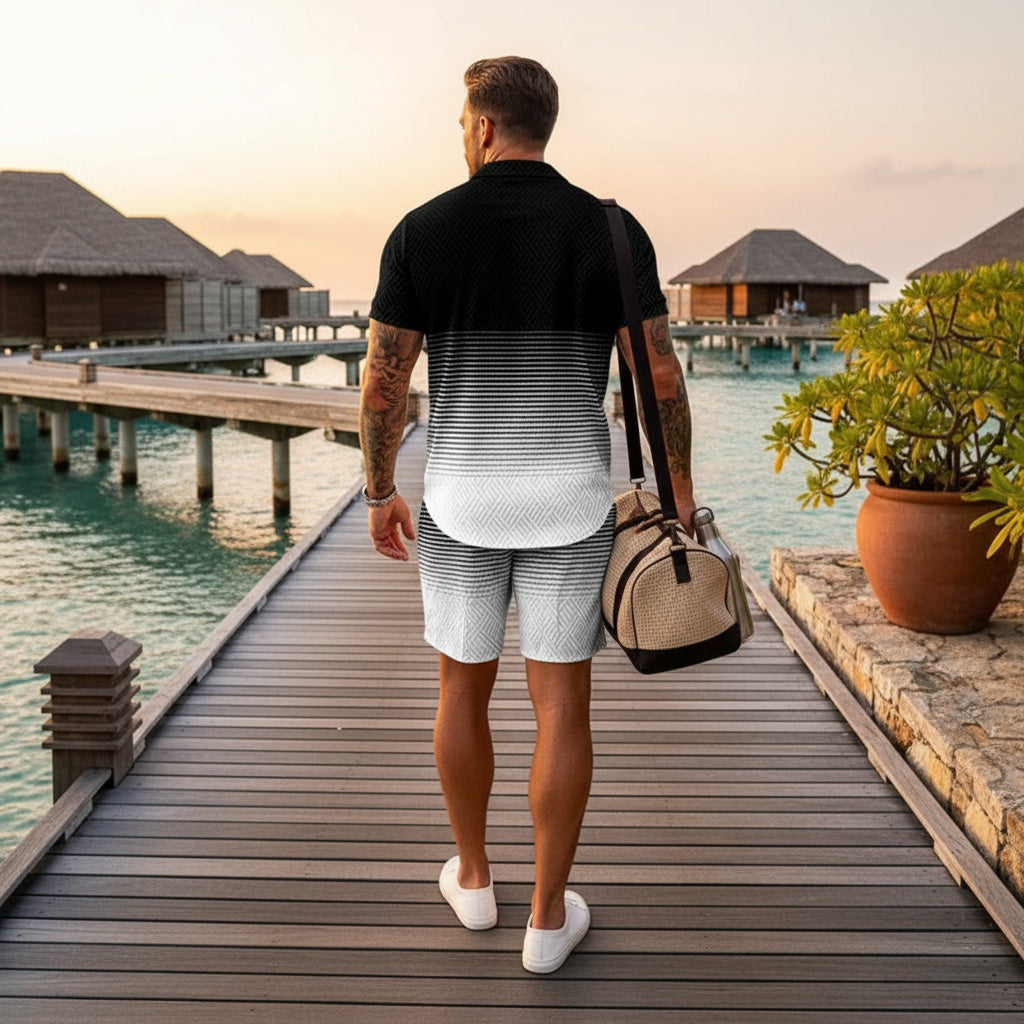 A man viewed from behind walking on a wooden boardwalk over water, wearing a black polo shirt with a white-to-gray gradient pattern and light gray shorts, while carrying a beige duffel bag.