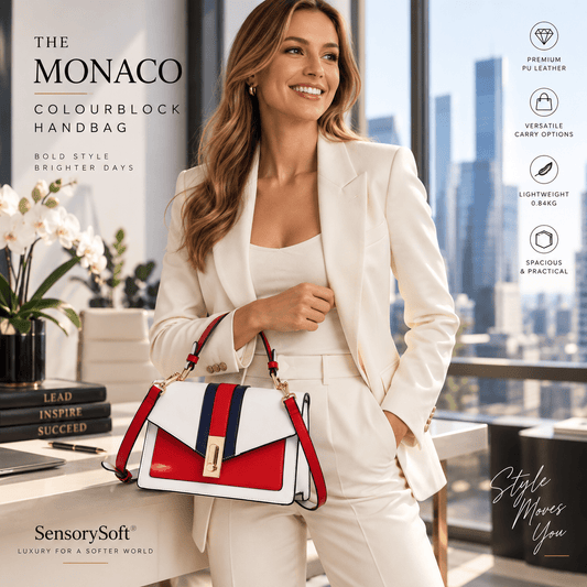 A woman in a white blazer and trousers holds a SensorySoft Monaco Colourblock Handbag. The handbag is white with red and navy blue stripes and a gold-tone clasp.