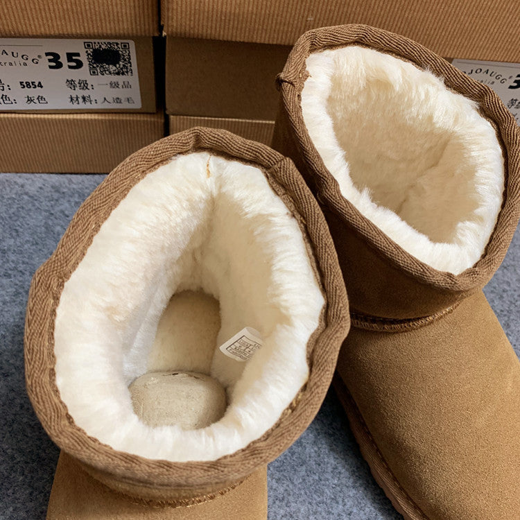 Brown winter boots with white fur lining on a gray surface, with a cardboard box in the background.