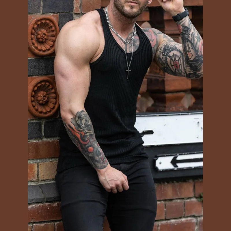 Man with tattoos wearing a black tank top against a brick wall.