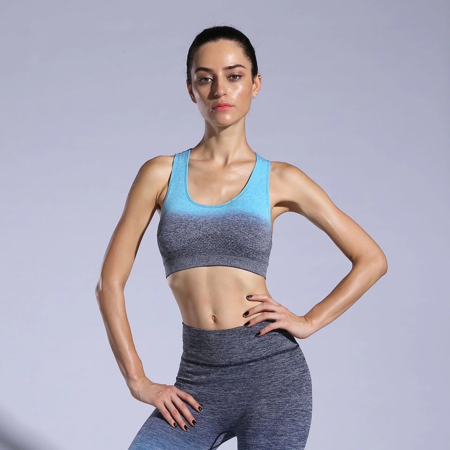 Woman wearing a blue and gray sports bra and leggings on a light gray background